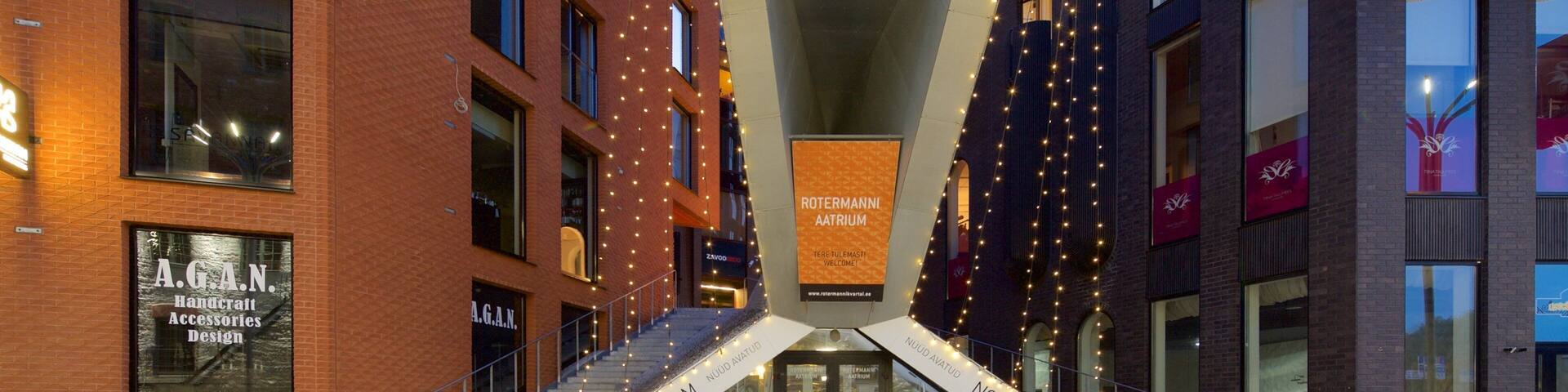 A modern urban street with brick buildings, a glass entrance, and decorative string lights.