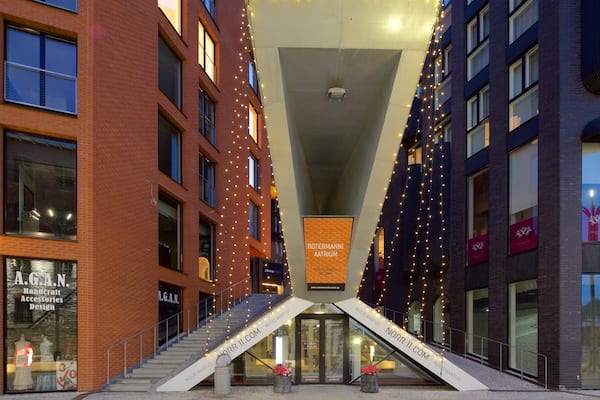 A modern urban street with brick buildings, a glass entrance, and decorative string lights.