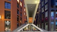 A modern urban street with brick buildings, a glass entrance, and decorative string lights.