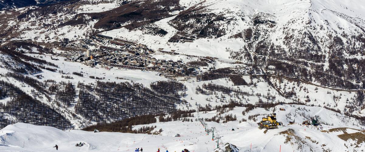 A snow-covered mountain landscape with ski slopes, a town, and a ski lift.