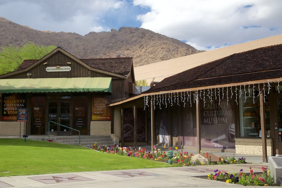 Museu Cultural Agua Caliente com toldo verde, rodeado por um jardim bem cuidado e montanhas ao fundo.