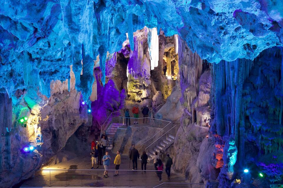A cave with colorful stalactites and stalagmites, a staircase, and visitors.