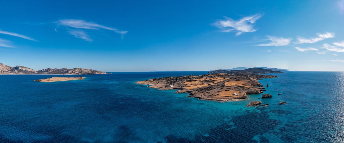 A coastal landscape with clear blue waters, rocky islands, and a distant mountain range.
