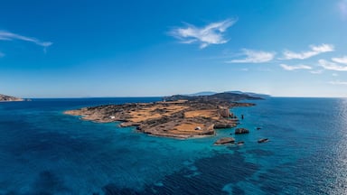 Paisagem costeira com águas azul-claras, ilhas rochosas e uma cadeia montanhosa ao longe.