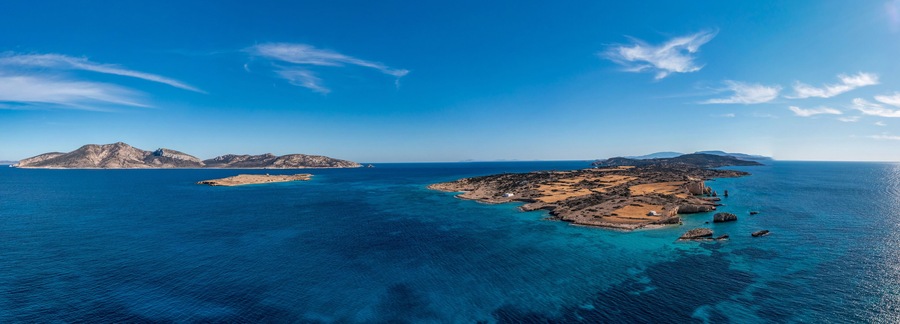 Paisaje costero con aguas azul cristalino, islas rocosas y una cadena montañosa distante.