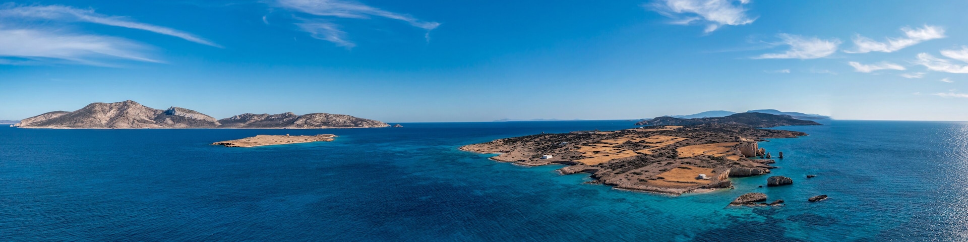 Paisagem costeira com águas azul-claras, ilhas rochosas e uma cadeia montanhosa ao longe.