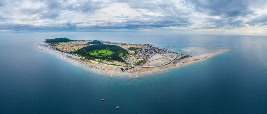 Vista aérea de una isla con playa, carretera y un pequeño bote en el agua.