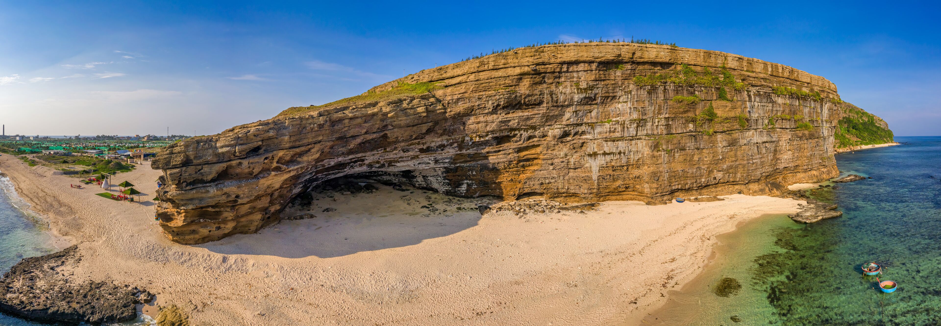 A large rock formation with a natural arch over a beach.