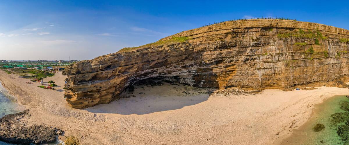 A large rock formation with a natural arch over a beach.
