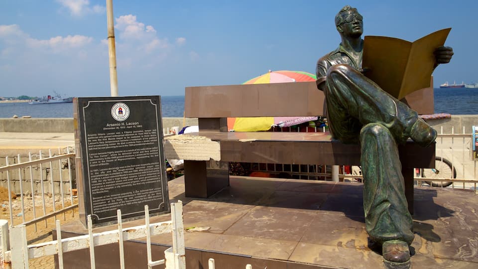 A statue of a man reading a book, a bench, and a sign with text.