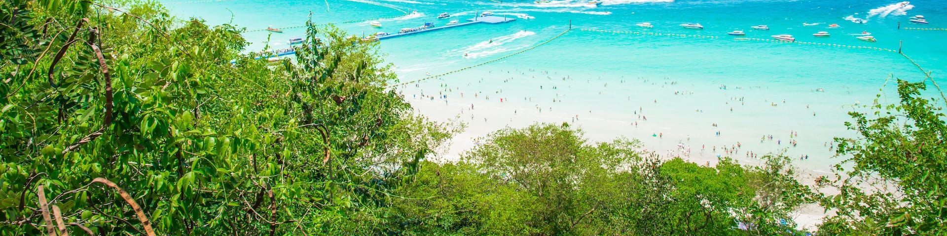 A coastal landscape with a beach, clear turquoise waters, and boats.