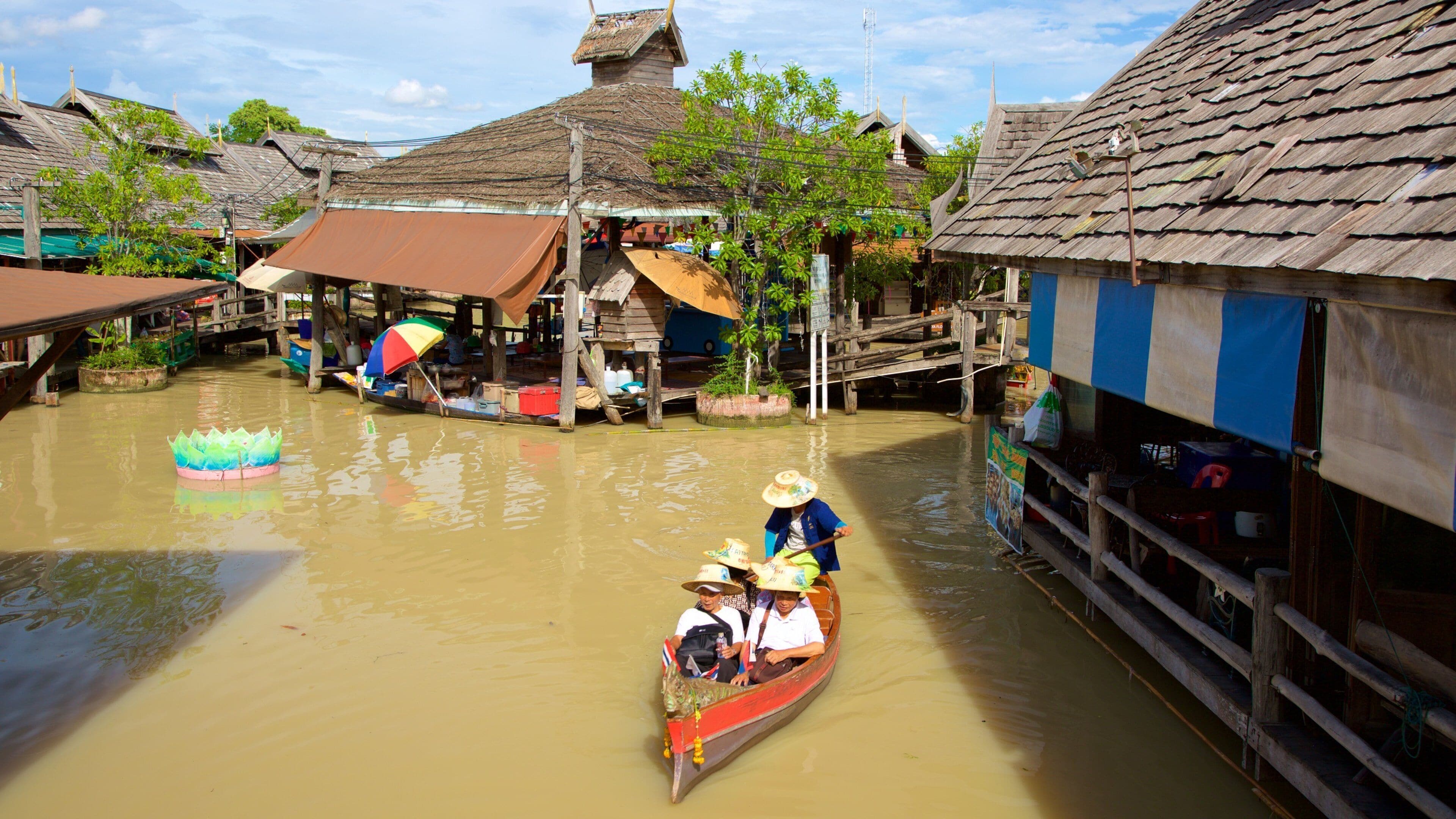A traditional boat on a river with wooden houses and a lotus float.