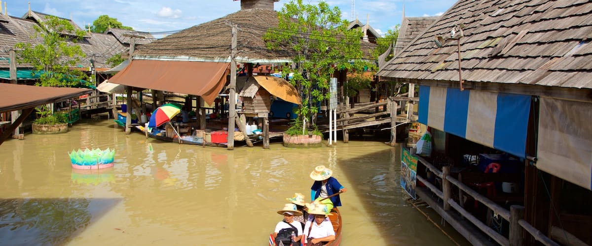 A traditional boat on a river with wooden houses and a lotus float.