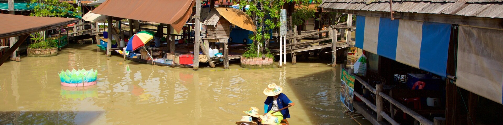 A traditional boat on a river with wooden houses and a lotus float.