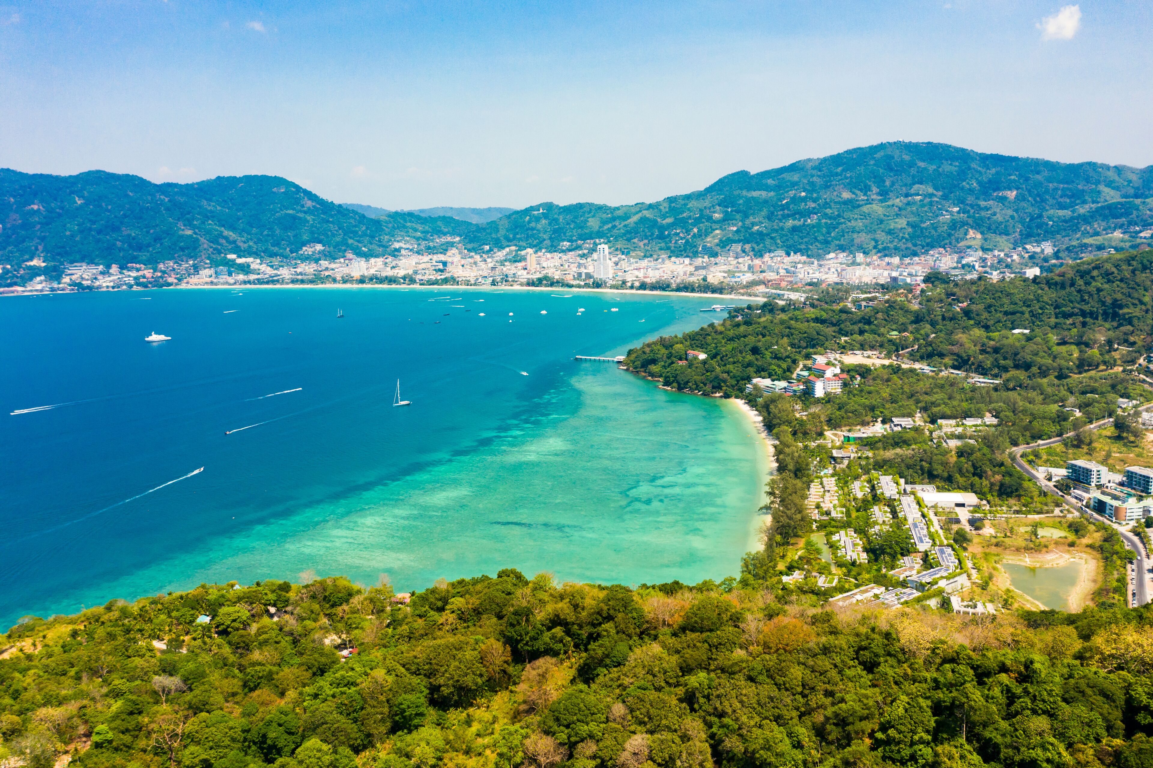 View from above, stunning aerial view of Patong city skyline in the distance and the beautiful Tri Trang Beach bathed by a turquoise and clear sea in the foreground, Phuket, Thailand.