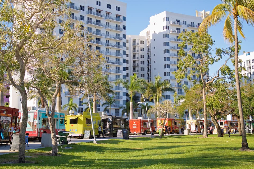 Un parque con césped verde, palmeras y camiones de comida.