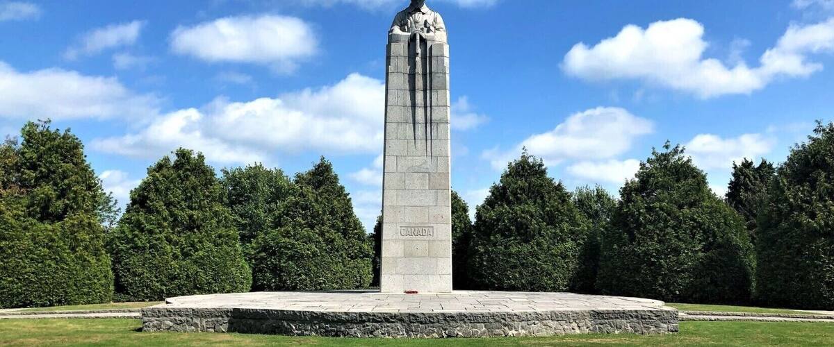 A tall monument with a plaque reading "CANADA" in a park with trees and a clear sky.