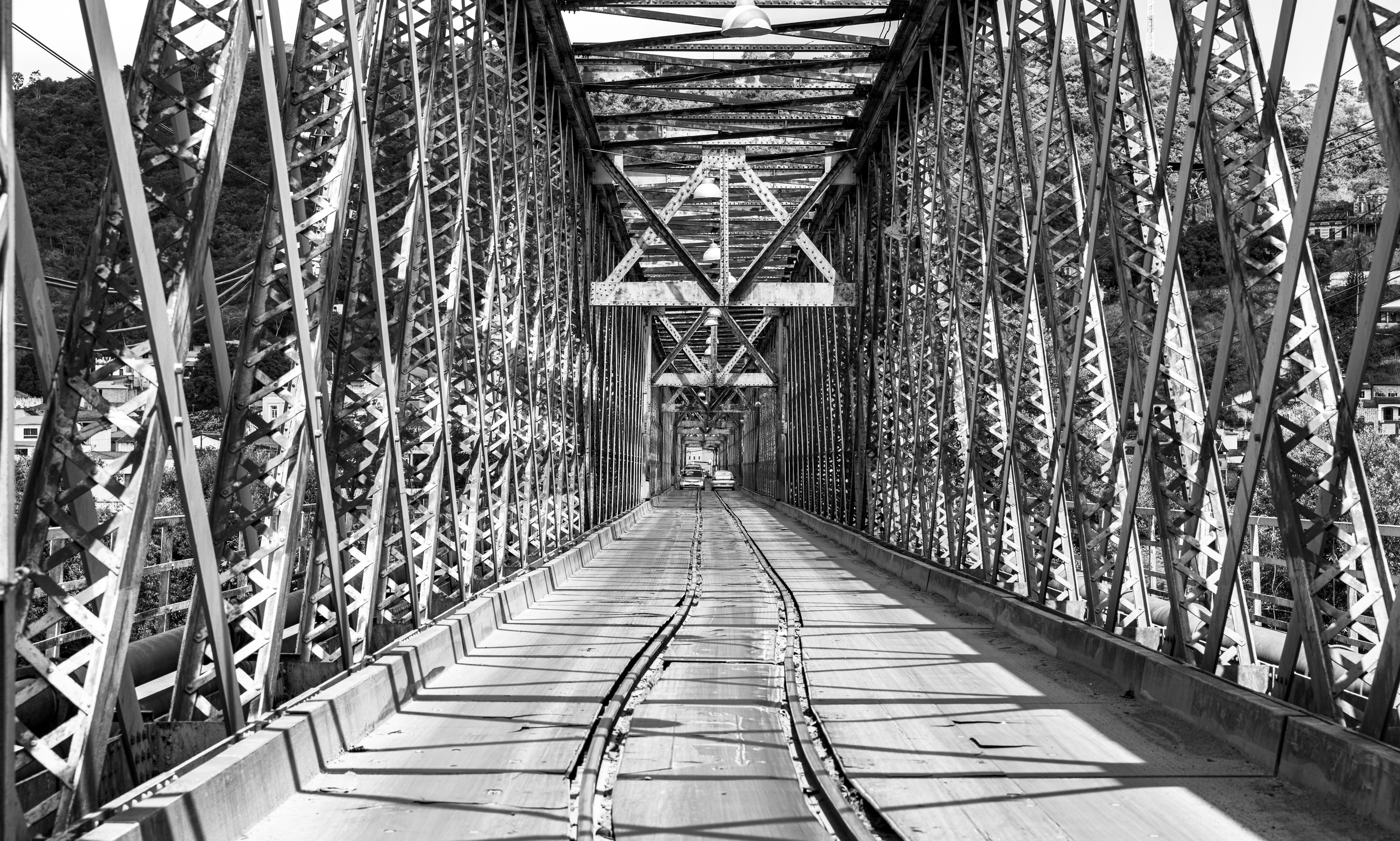 A black and white view of a steel bridge with a truss structure, featuring a concrete walkway and metal railings.