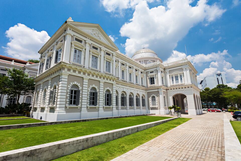 A large, classical building with a dome and columns, surrounded by well-maintained lawns and a paved walkway.