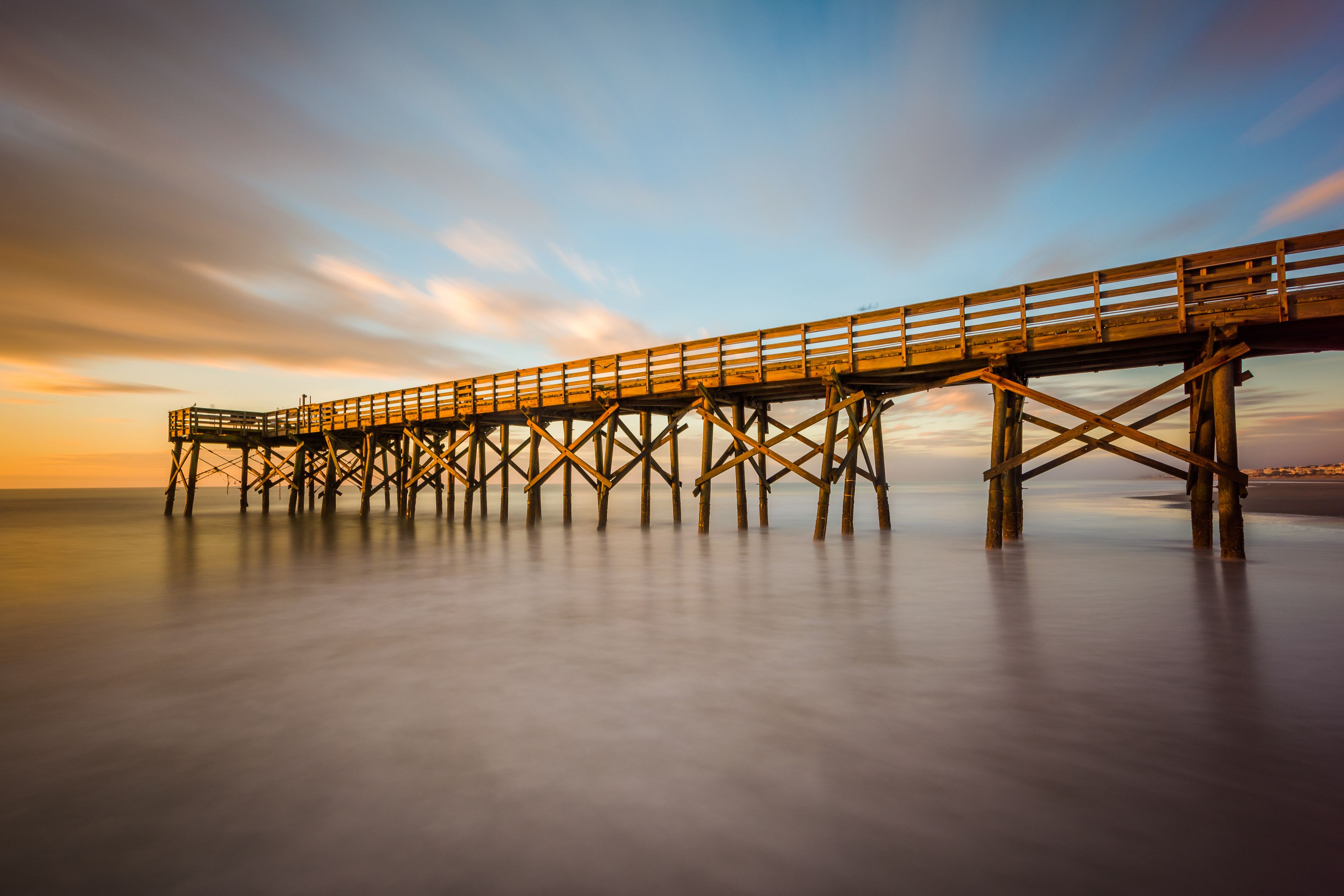 A wooden pier extending into calm waters at sunset.