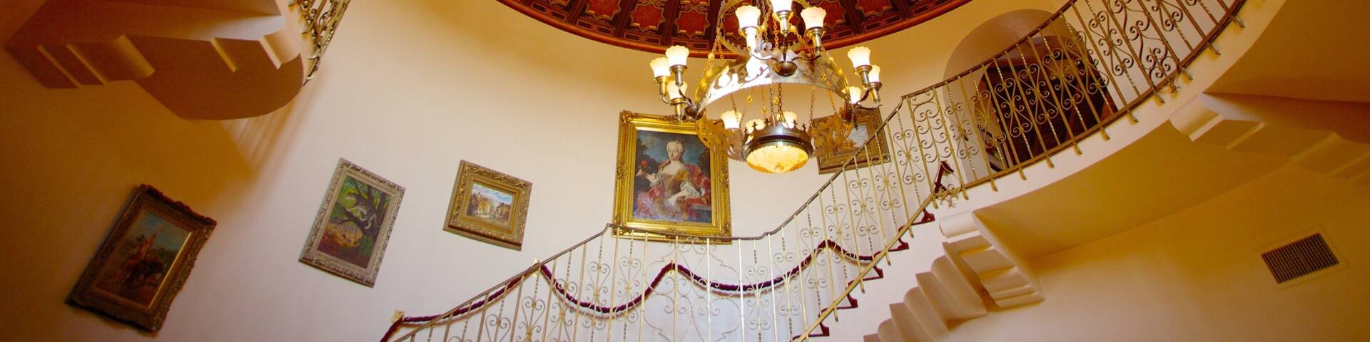 Una imponente escalera ornamentada con una cúpula decorada en rojo y oro, y un candelabro.