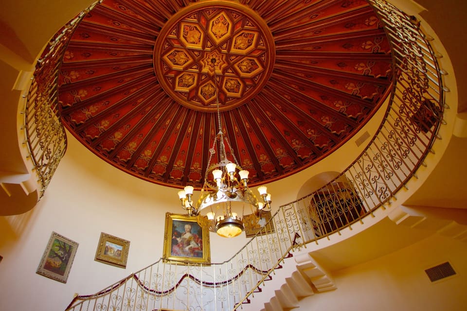 A grand, ornate staircase with a red and gold patterned dome ceiling and a chandelier.