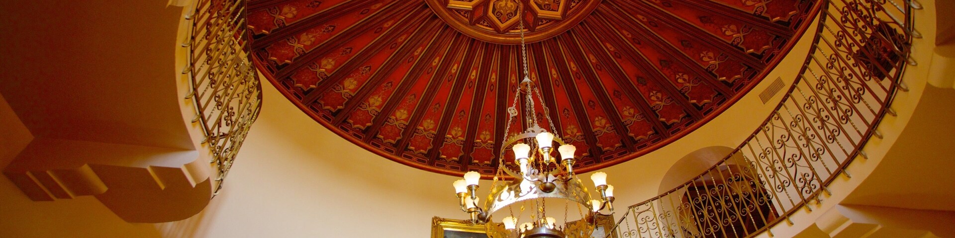 Una imponente escalera ornamentada con una cúpula decorada en rojo y oro, y un candelabro.