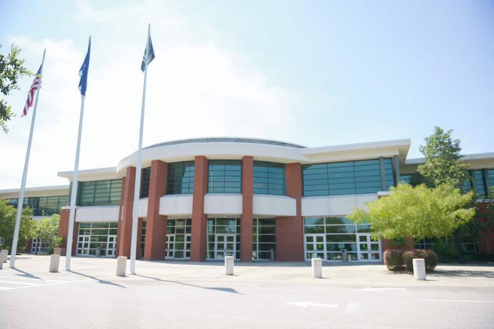 A modern building with large windows and a curved facade, surrounded by flagpoles and a clear sky.