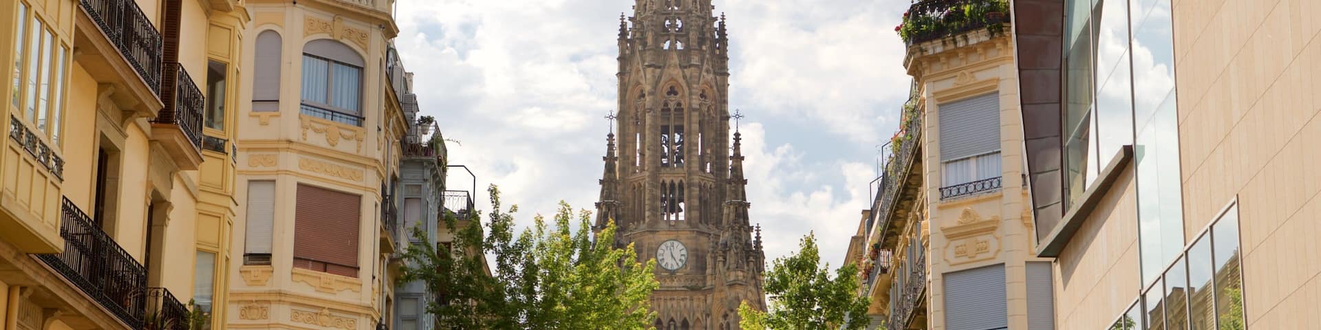 A cathedral with a tall spire, surrounded by buildings with balconies and trees.