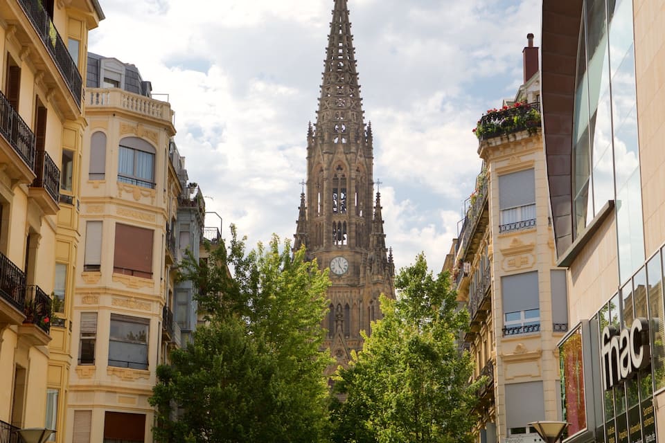A cathedral with a tall spire, surrounded by buildings with balconies and trees.