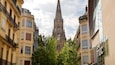 A cathedral with a tall spire, surrounded by buildings with balconies and trees.