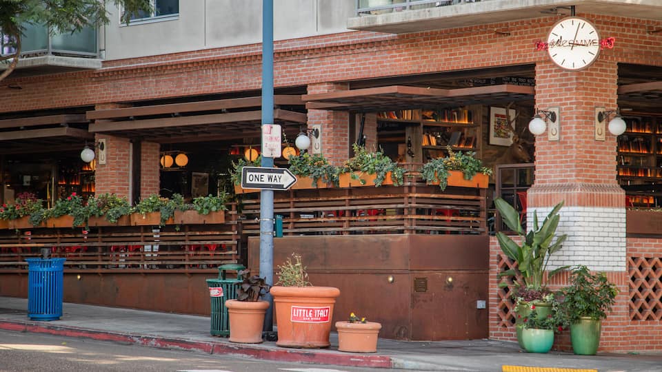 A brick building with a 'ONE WAY' sign, outdoor seating, and potted plants.