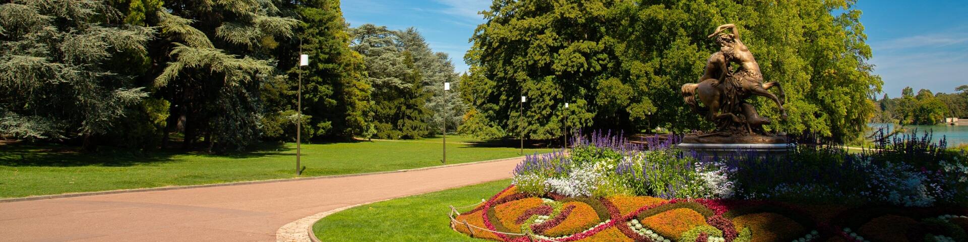 A park with a statue, trees, and a flower garden.