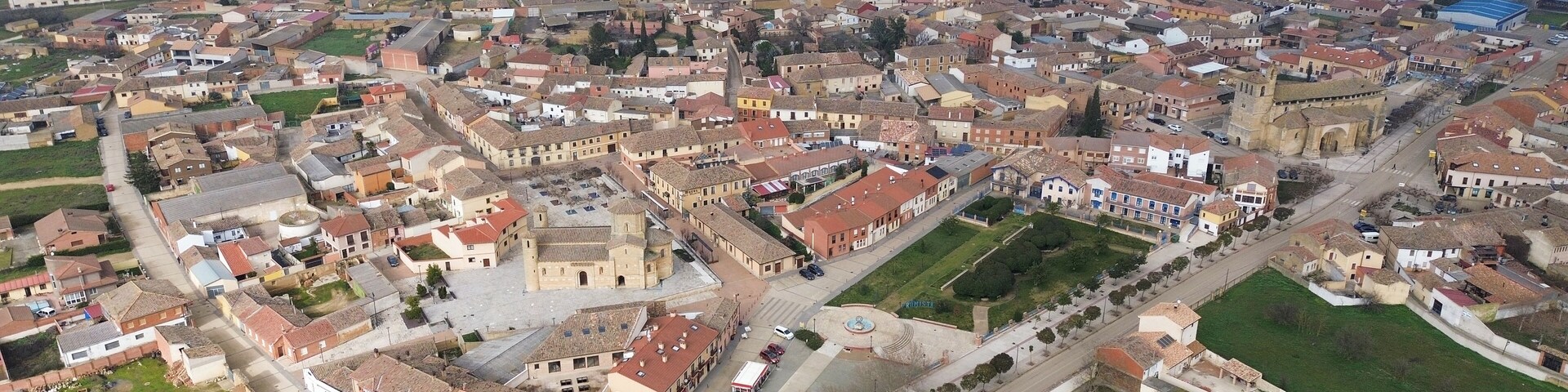 Vista aérea de uma cidade com uma praça central, edifícios ao redor e campos.
