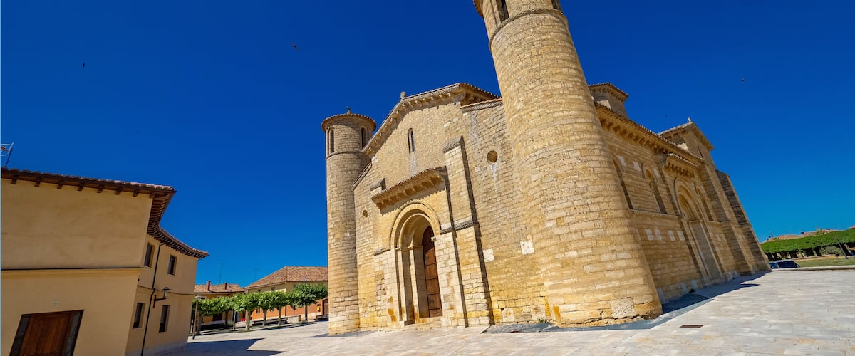 A historic stone church with a prominent bell tower and arched entrance under a clear blue sky.