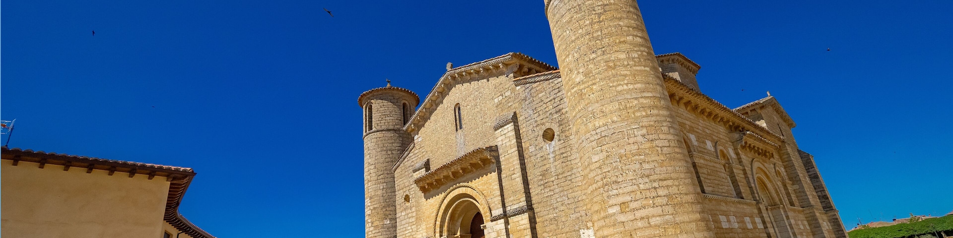 A historic stone church with a prominent bell tower and arched entrance under a clear blue sky.