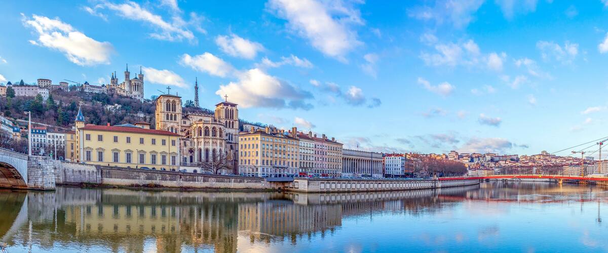 Ein Fluss mit einer Brücke, historische Gebäude und ein Hügel mit einer Kirche.