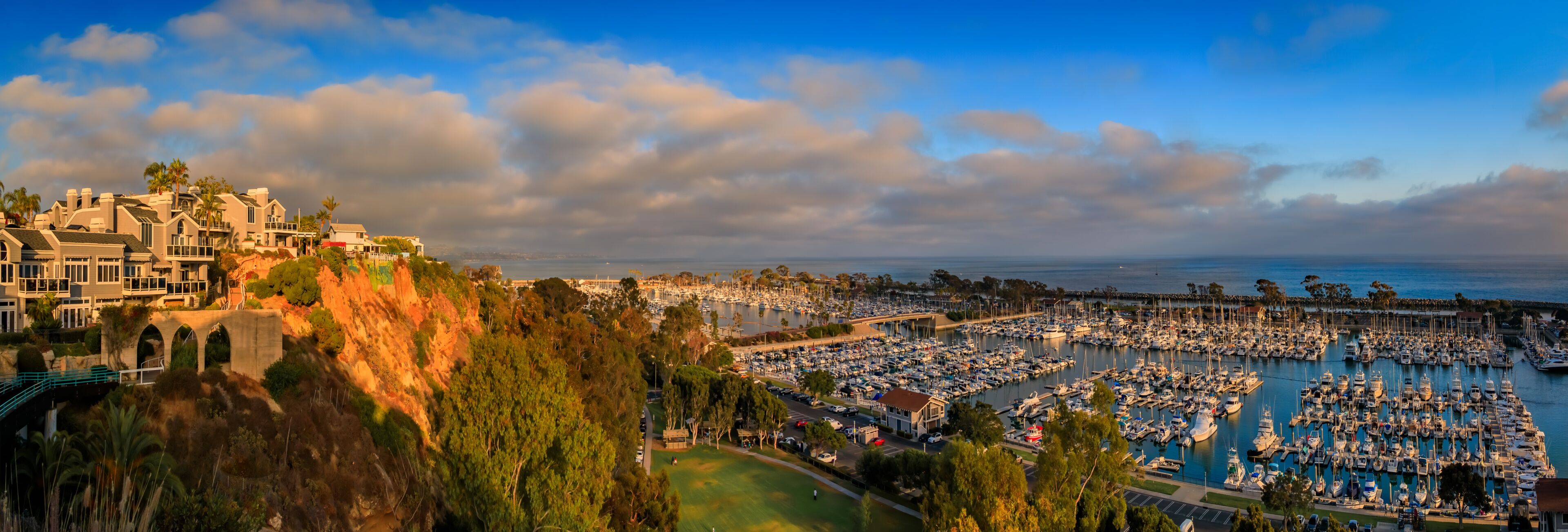 A marina filled with boats, a coastal town with buildings, and a clear sky.