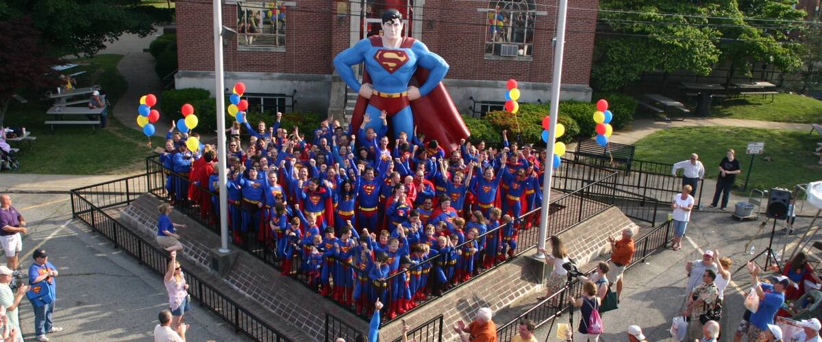 Superman Statue featuring a square or plaza and a statue or sculpture as well as a large group of people