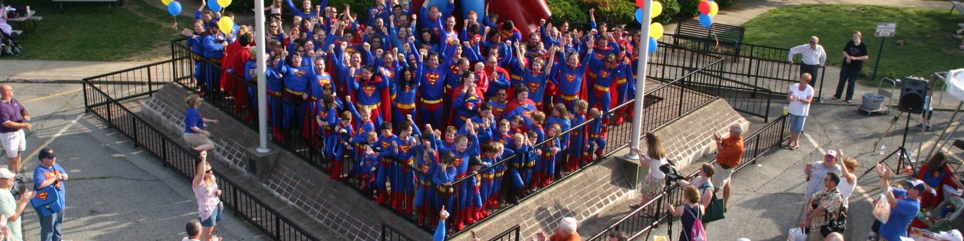 Superman Statue featuring a square or plaza and a statue or sculpture as well as a large group of people