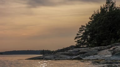 A sunset over a calm lake with a rocky shoreline and trees.