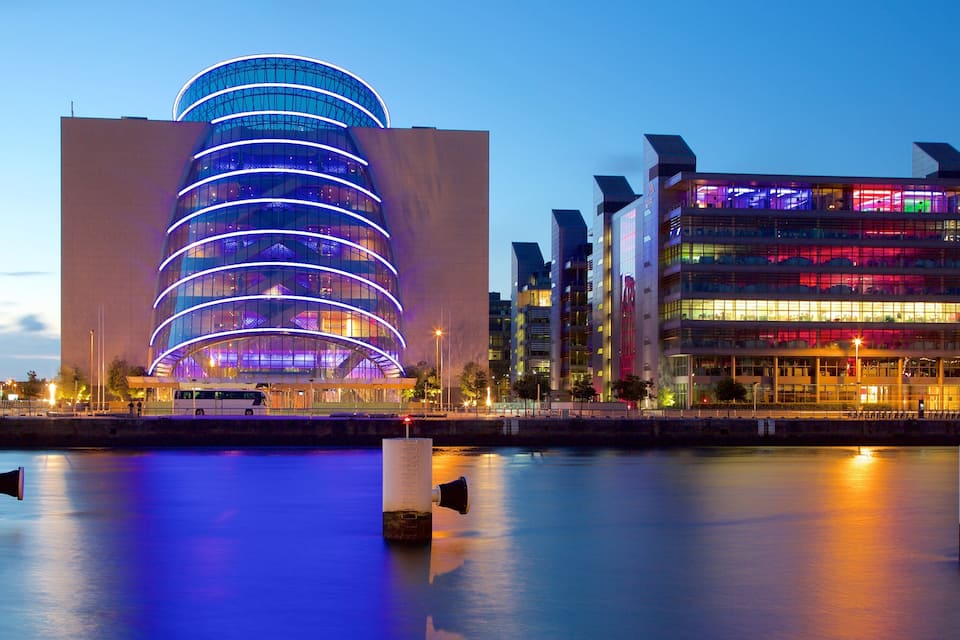 A modern building with a curved glass facade and a rectangular structure with colorful lighting.
