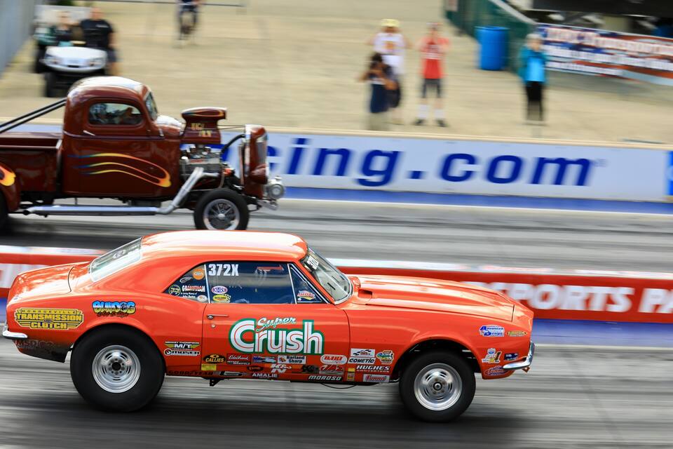 Een klassieke oranje raceauto met diverse sponsorstickers, rijdt over een circuit met een onscherpe achtergrond.