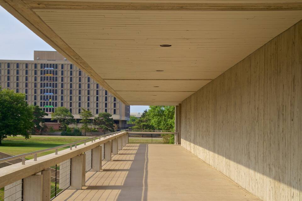 Une allée couverte offrant une vue sur un bâtiment moderne et une zone verdoyante.