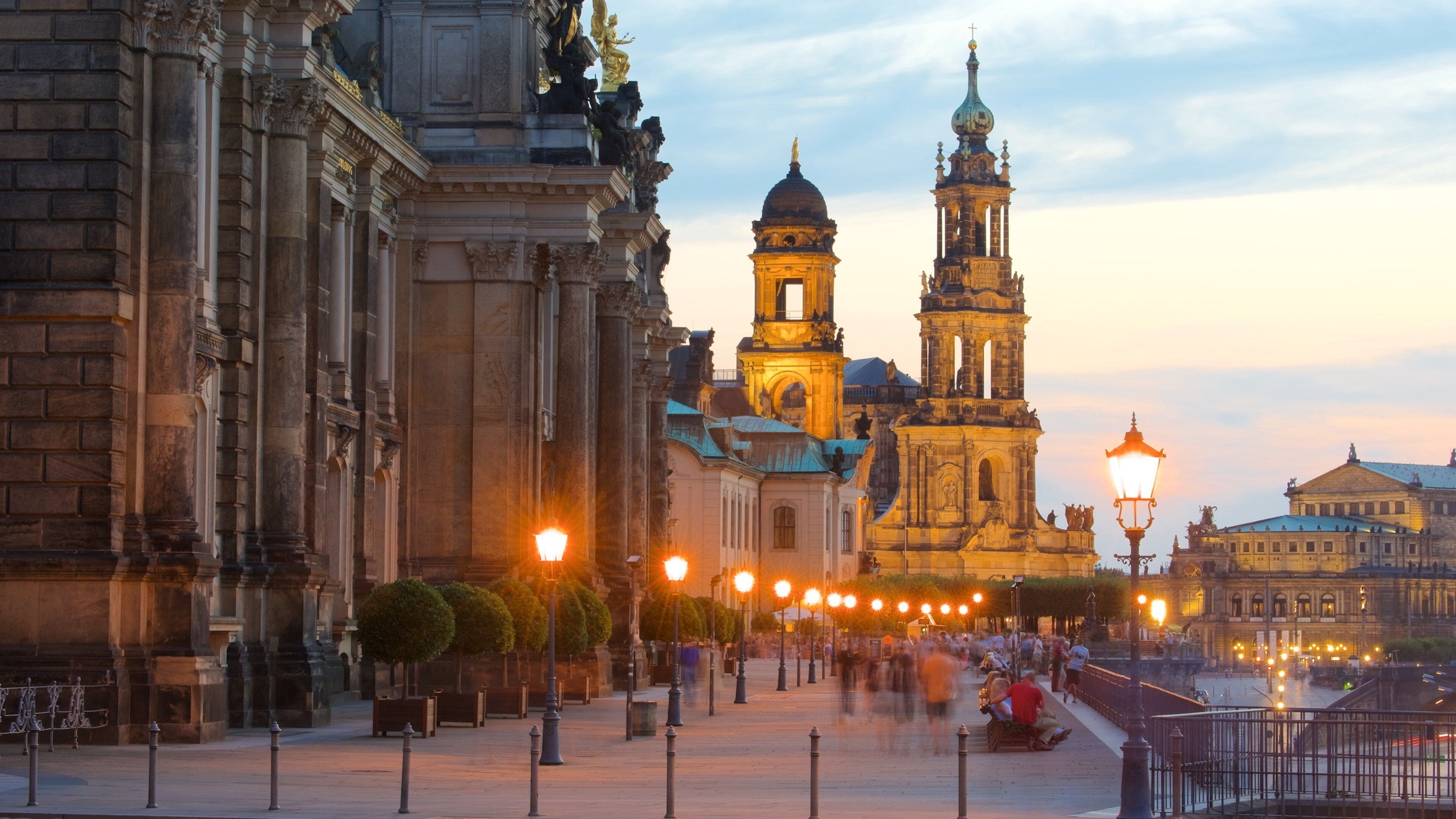 Una plaza histórica con edificios ornamentados, una imponente torre del reloj y una calle bien iluminada.