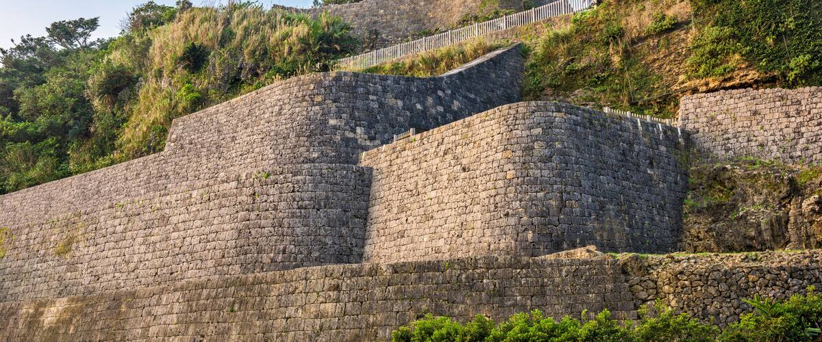A stone fortification with a curved wall, surrounded by greenery and a clear blue sky.