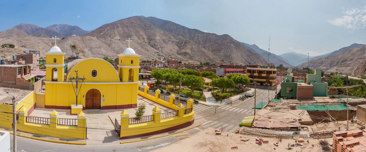 A yellow church with two towers, a street, and mountains in the background.