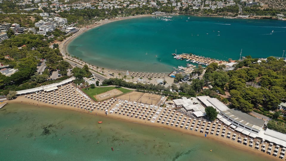An aerial view of a coastal area with a beach, a marina, and surrounding residential buildings.