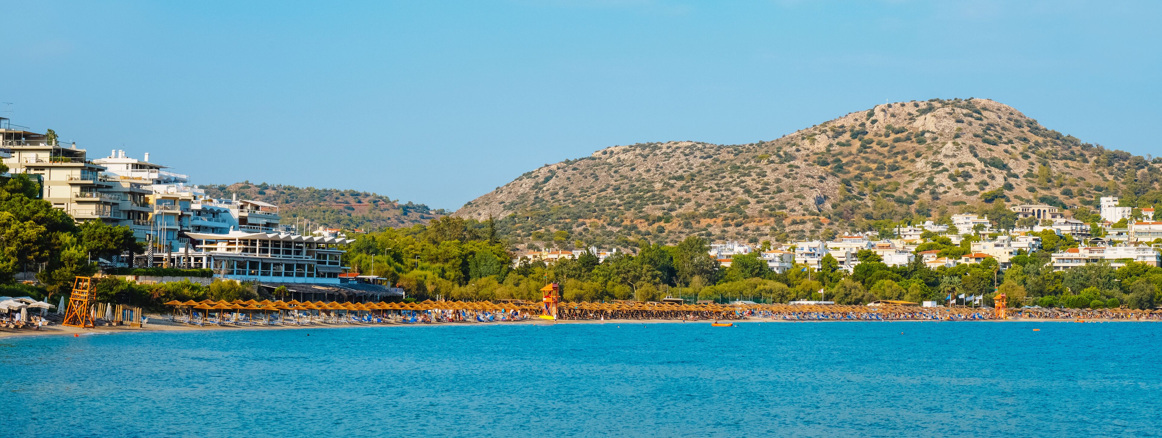 A coastal town with a beach, a mountain, and buildings along the shore.