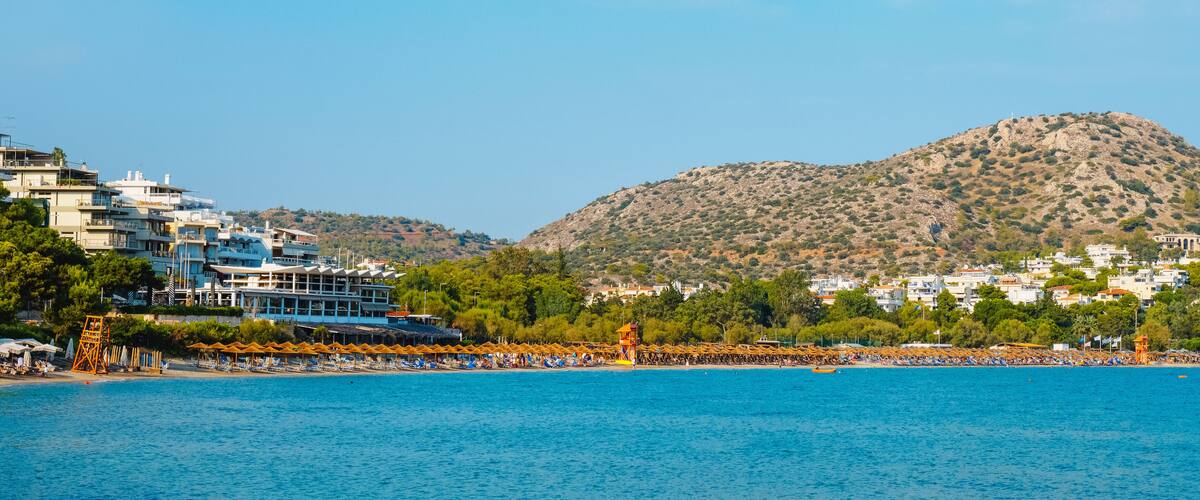 A coastal town with a beach, a mountain, and buildings along the shore.
